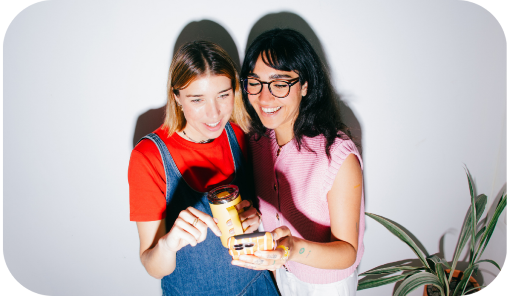 Ki Jugend Werkstatt Junge Menschen zeigen auf ein Handy mit grauer Wand und Pflanze im Hintergrund